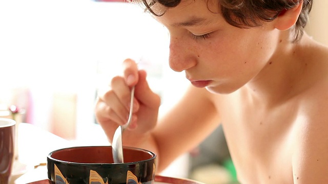 一个十几岁的小男孩一边玩一边吃着一碗麦片视频素材