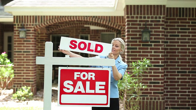 房地产经纪人在房子上挂上“出售”的牌子。视频素材