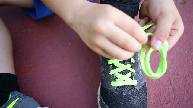一个蹒跚学步的小男孩试图在户外的人行道上系鞋带。视频下载
