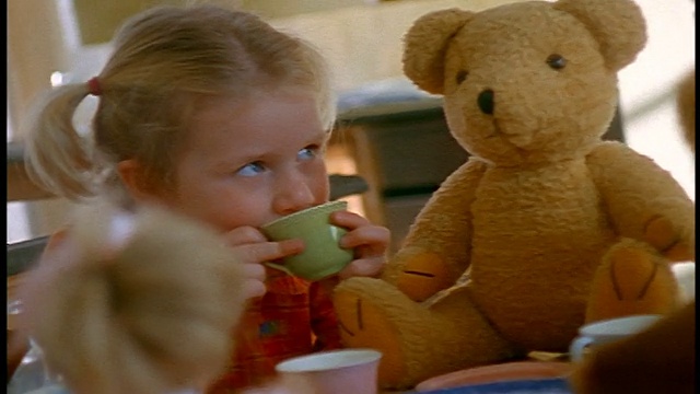 小金发女孩在茶会上用茶杯喝东西，还有玩具娃娃和泰迪熊视频素材