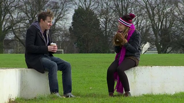 一对夫妇讲笑话与咖啡在公园在冬天宽镜头视频下载