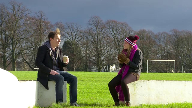 一对夫妇在冬天的公园里喝咖啡聊天宽镜头视频素材