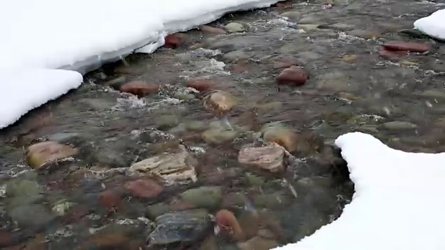近距离拍摄的彩色岩石在河与雪覆盖的河岸期间，大雪。视频素材