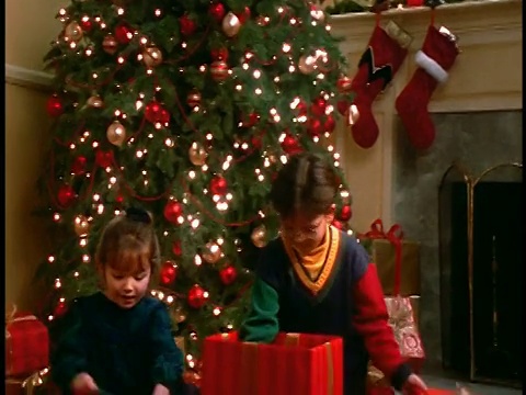 女孩+男孩在客厅的圣诞树旁打开圣诞礼物+拥抱洋娃娃+泰迪熊视频素材