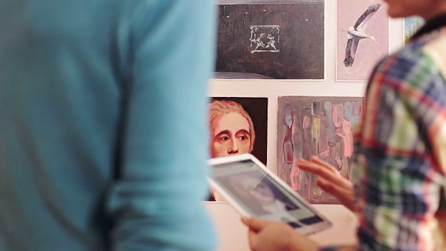 一名艺术家使用数码板向一名年轻女子展示一幅画作。视频下载