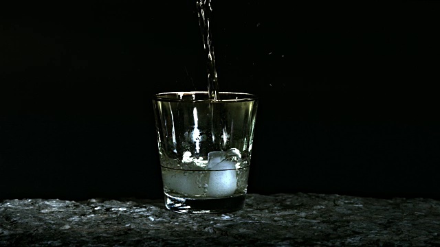 在黑色背景下，威士忌被倒入装有冰块的玻璃杯中的慢镜头视频下载