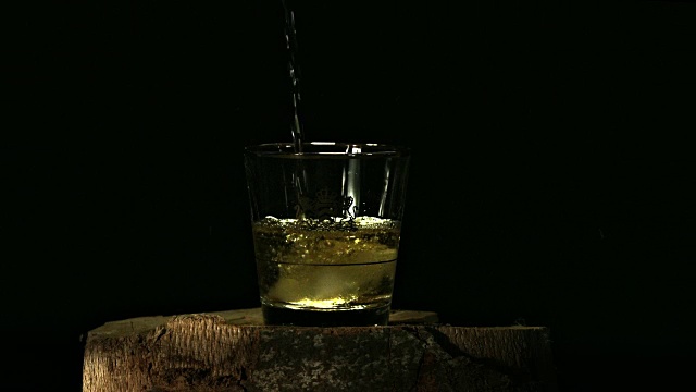 在黑色背景下，威士忌被倒入装有冰块的玻璃杯中的慢镜头视频下载