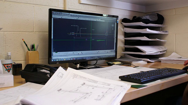 绘图员手翻建筑图纸前景，机架焦点到计算机显示器上的CAD效果图背景视频素材