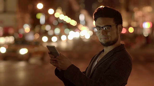 城市生活方式的肖像，年轻的亚洲男子使用平板电脑设备在晚上在城市的户外视频素材
