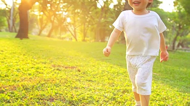 高清:快乐的小男孩在公园里奔跑，背景是夕阳(慢镜头)。视频素材