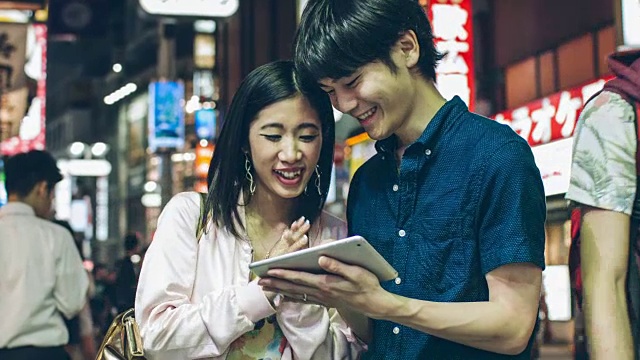 一对年轻的日本夫妇用数码平板电脑玩得很开心视频素材