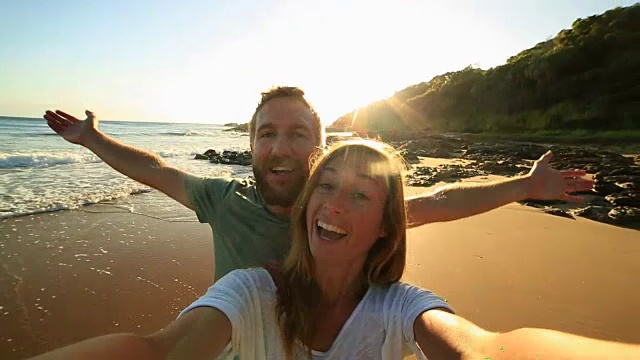 一对快乐的年轻夫妇在海滩上拍自拍照视频下载