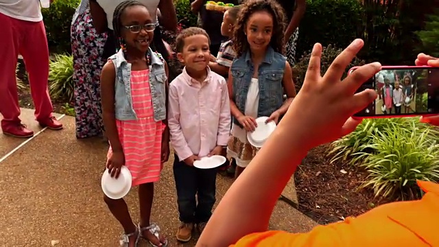 一个小男孩在家庭庆典期间用智能手机给堂兄弟姐妹拍照视频下载