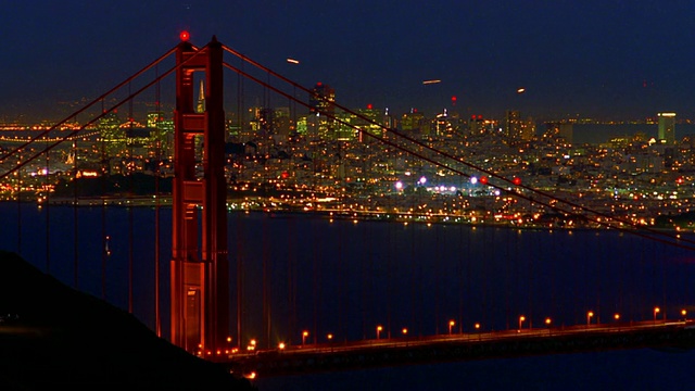中景延时拍摄金门大桥交通，旧金山天际线为背景，夜间/延时拍摄飞机在上空视频素材