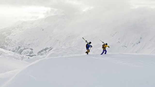 两个偏远地区的滑雪者扛着滑雪板沿着山脊行进视频素材