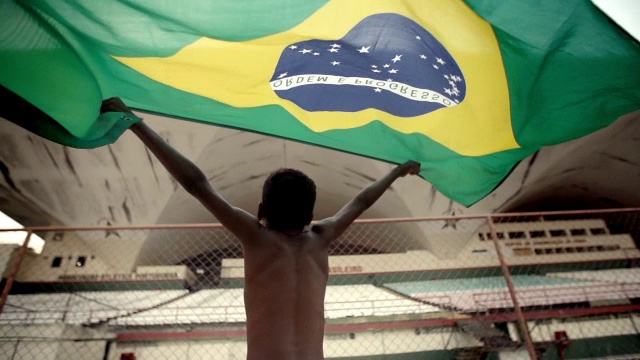 在足球场上，一个小男孩在慢镜头中得意洋洋地将巴西国旗举过头顶视频下载
