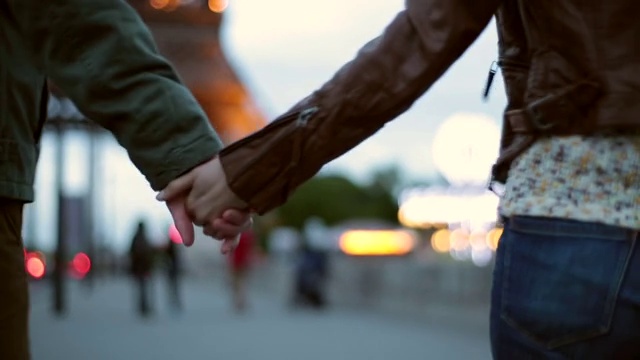手持式近距离后方跟踪拍摄年轻的男子和女子手牵手，而走在巴黎的埃菲尔铁塔在黄昏视频下载