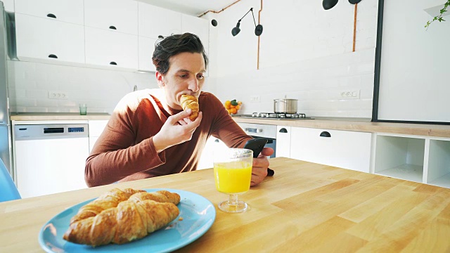 男人一边吃早餐一边看手机。视频素材