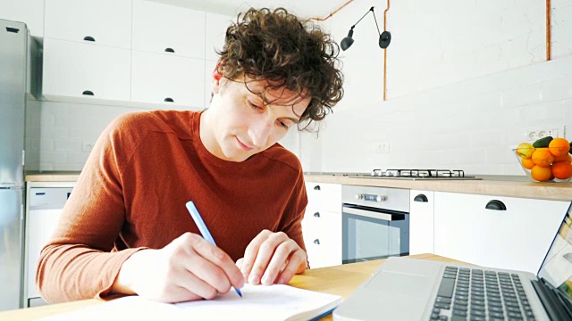 年轻人边用笔记本电脑边做笔记。视频素材