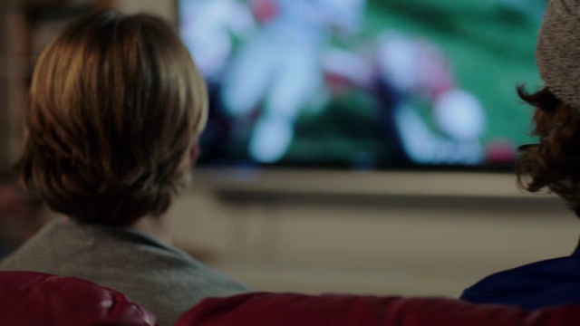 一群年轻的成年男性和女性一起庆祝观看电视上的体育运动近距离在多利肩上视频素材