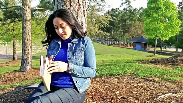 一位拉丁裔女性在公园户外阅读。视频下载