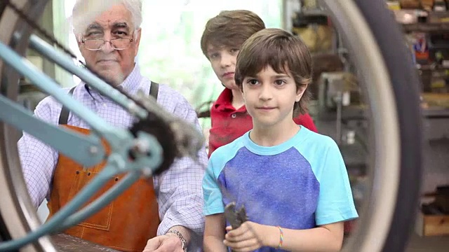 孙子在车间和爷爷一起修自行车。视频素材