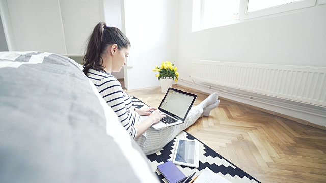 一个舒适的年轻女人在家里用笔记本电脑。视频素材