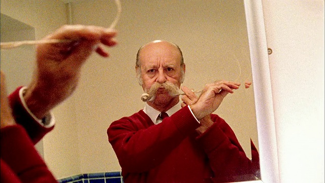 中等拍摄的高级男子解开长胡子，并在镜子中卷起来视频素材