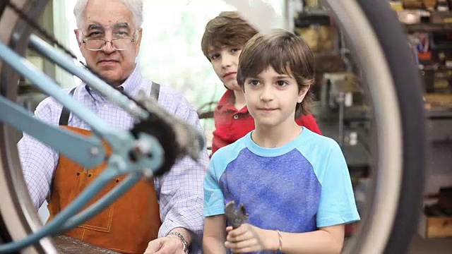 孙子在车间和爷爷一起修自行车。视频素材