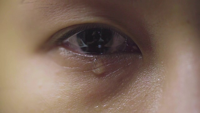 特写:眼泪从眼睛里流出，沿着脸颊流下。悲伤的受虐女性棕色眼睛哭泣，亚洲模特。视频下载