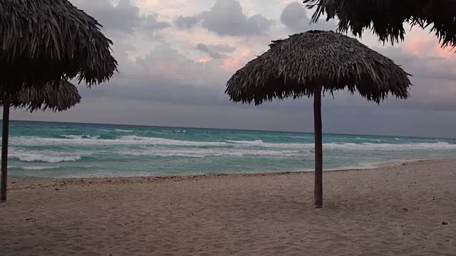 巴拉德罗海滩在一个恶劣的热带天气。夕阳伴着彩云，沙滩上还有一些棕榈叶伞。巴拉德罗,马坦萨斯,古巴视频下载