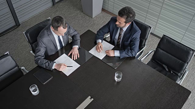 在会议室的桌子上方，两名商人正在签署合同并握手视频下载