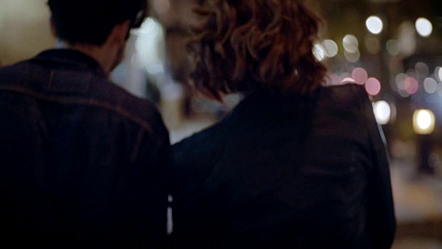 一对兴奋的年轻夫妇手牵着手走在夜晚的城市人行道上。视频下载