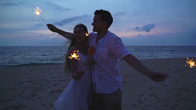 4K:幸福的情侣在日落时分在海滩上点燃火花，享受自由。视频下载
