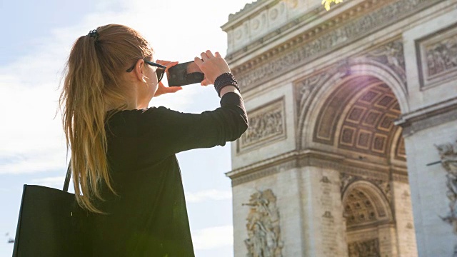 年轻的女游客走在巴黎的街道上，拍下凯旋门的照片视频素材