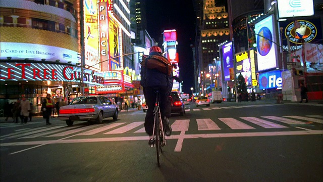寬鏡頭跟蹤拍攝的自行車信使在晚上穿過時代廣場/紐約視頻下載