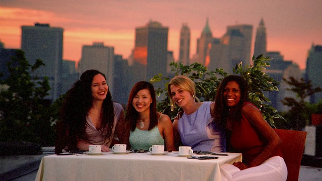 Medium拍摄了四名年轻女性坐在屋顶餐桌上，拿着咖啡杯，摆姿势/纽约视频下载