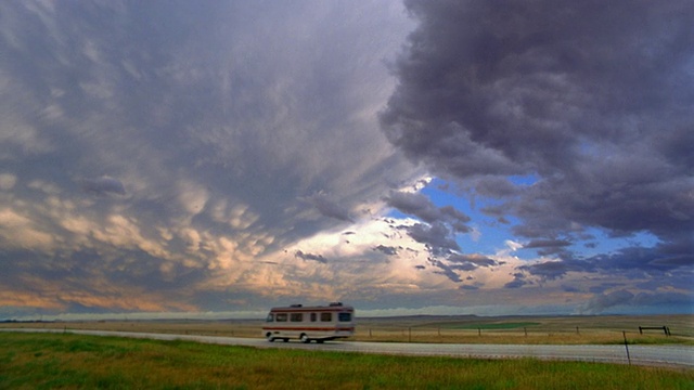 宽镜头的休闲车辆驾驶在乡村道路上/轻和黑暗的云在背景/内华达州视频下载