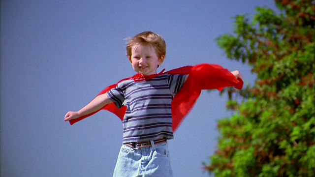 中镜头变焦男孩在红色的超级英雄斗篷转向w/斗篷吹在风视频下载
