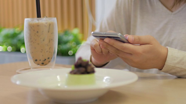 咖啡馆里，一位女士在喝咖啡时，在木桌上触摸智能手机视频下载