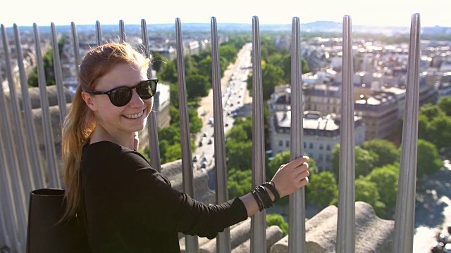 一名游客站在巴黎凯旋门上俯瞰整个城市，对着镜头微笑视频素材