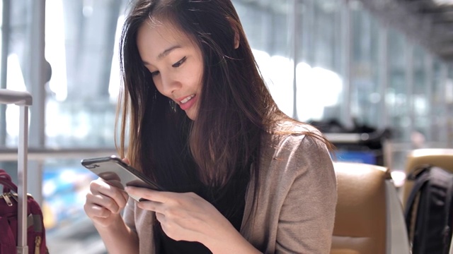 微笑的年轻亚洲女子在机场使用智能手机视频下载
