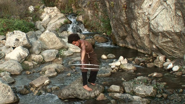 加州，赤裸上身的男子站在溪流中间的岩石上，绕着身体转呼啦圈，男子放下呼啦圈视频下载