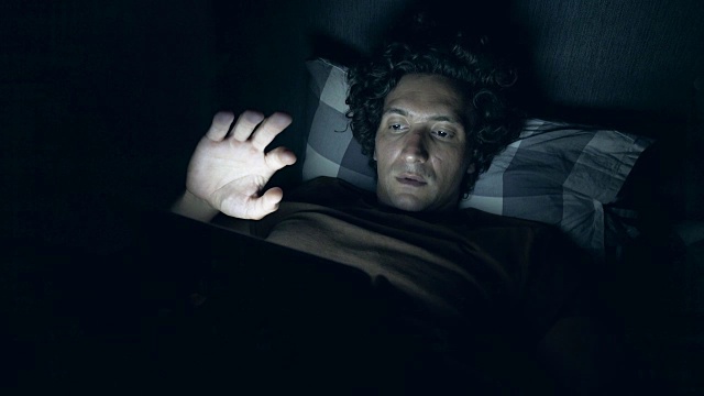 一头卷发的年轻人在床上用数码平板电脑。视频素材