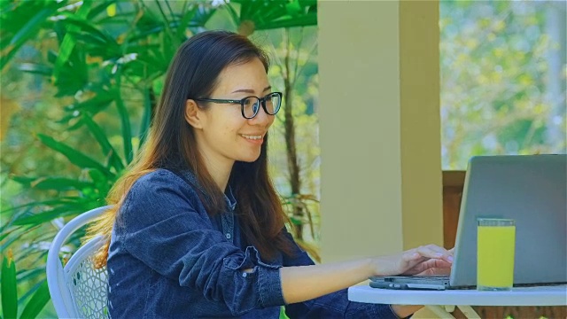微笑的年轻女子打字在笔记本电脑在花园里视频素材