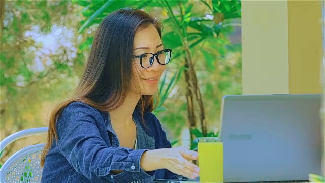 微笑的年轻女子打字在笔记本电脑和喝果汁在花园里视频素材
