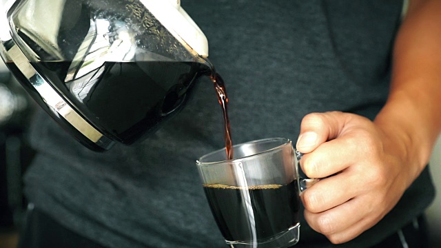 食物电影图片:一个男人在家里从玻璃壶倒一杯热咖啡在早上。视频素材