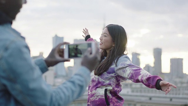 快乐的年轻亚洲女人在屋顶上摆姿势与摄影师与智能手机视频素材