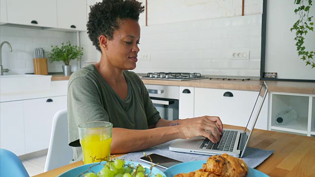一个女人坐在厨房里用笔记本电脑。视频素材