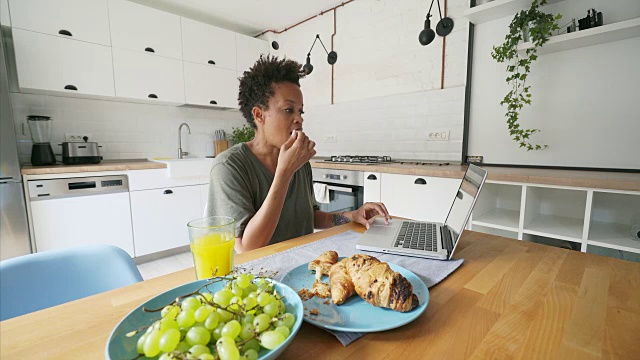 女性一边吃早餐一边用笔记本电脑工作。视频素材